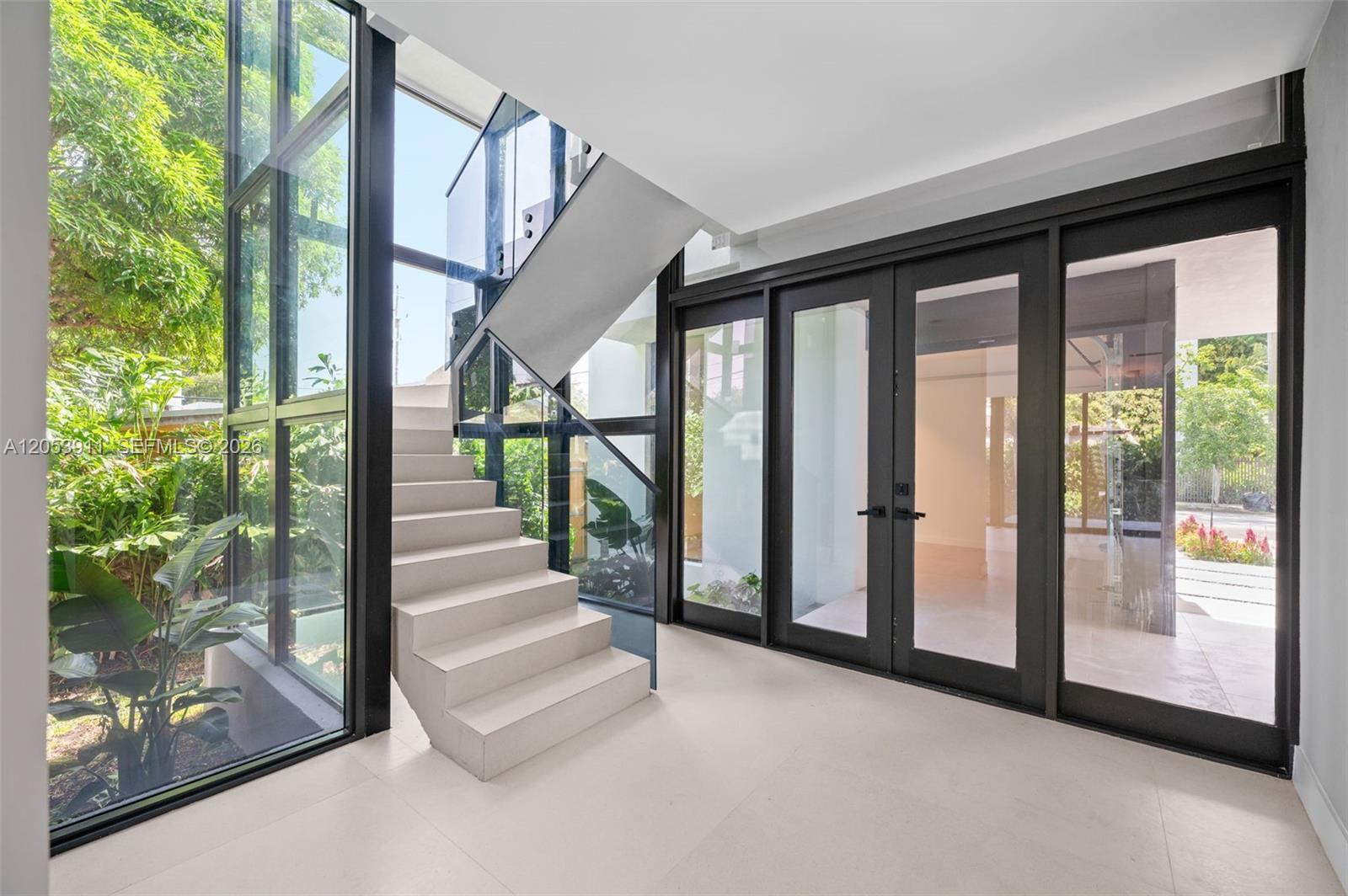 A modern entryway features a floating staircase, glass walls, and black-framed double doors — 3310 Elizabeth St, Miami FL 33133, MIAMI, FL