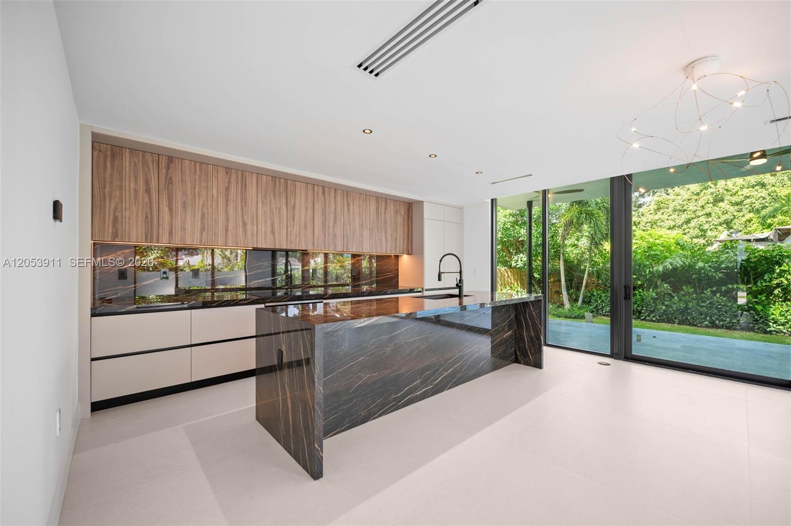 A modern kitchen features dark marble countertops, wood-toned upper cabinets, and floor-to-ceiling glass sliding doors — 3310 Elizabeth St, Miami FL 33133, MIAMI, FL