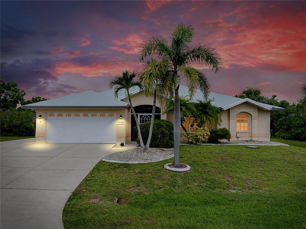 A single-story house with a two-car garage, palm trees, and a sunset sky background — 15140 LYNEBURG AVENUE, PORT CHARLOTTE, FL