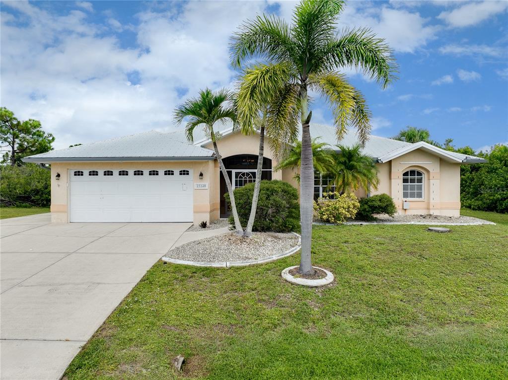 A single-story house with a white garage, palm trees, and a beige stucco exterior — 15140 LYNEBURG AVENUE, PORT CHARLOTTE, FL