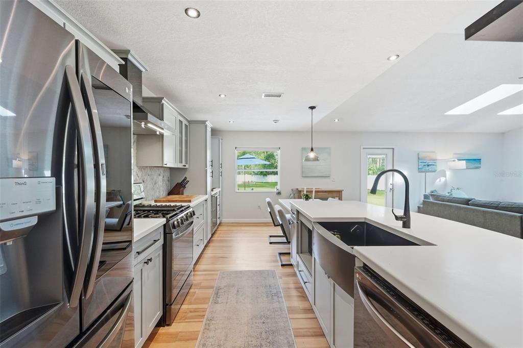 A modern kitchen features light gray cabinets, stainless steel appliances, and a large farmhouse sink — 18909 JEBERT DRIVE, ARIPEKA, FL