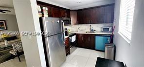 A kitchen with dark wood cabinets, stainless steel appliances, and white tile flooring — TAMARAC, FL