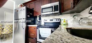 A kitchen features dark wood cabinets, stainless steel appliances, and granite countertops — TAMARAC, FL