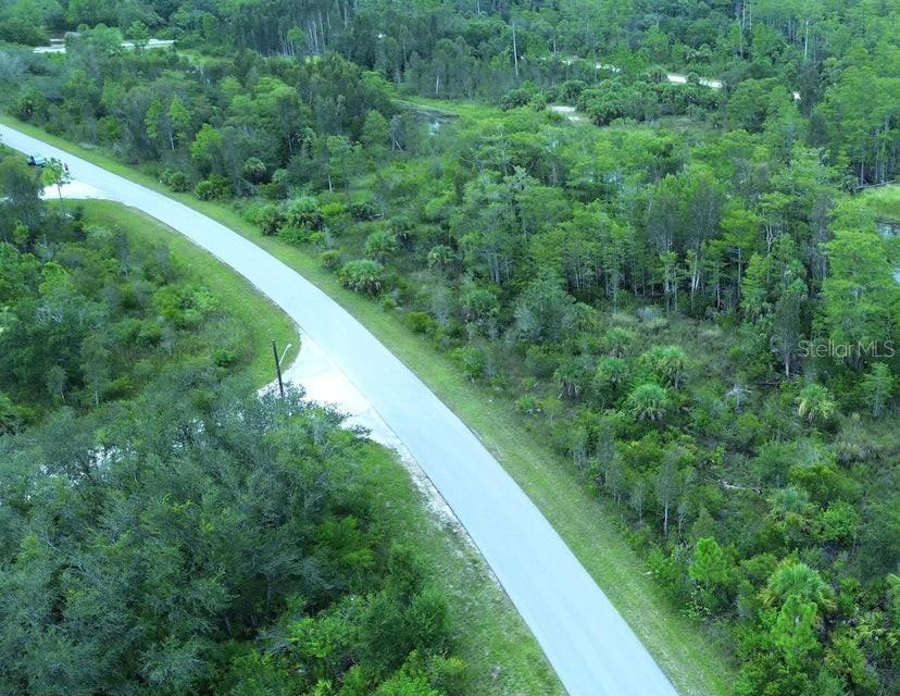 An aerial view shows a paved road winding through a dense, wooded, undeveloped landscape — 486 WESTCHESTER DRIVE, LEHIGH ACRES, FL