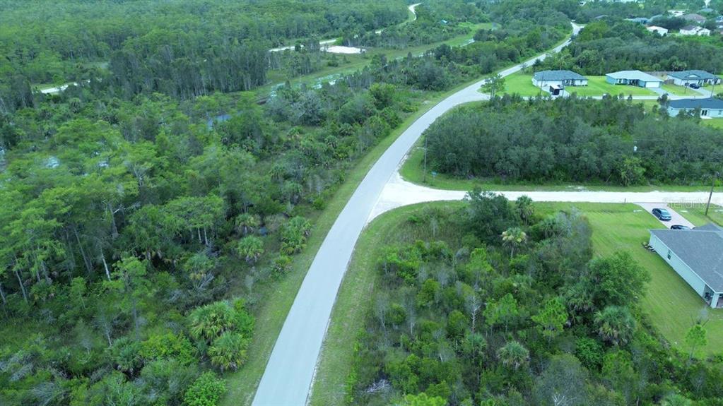 An aerial view shows a paved road winding through a wooded area with nearby houses — 486 WESTCHESTER DRIVE, LEHIGH ACRES, FL