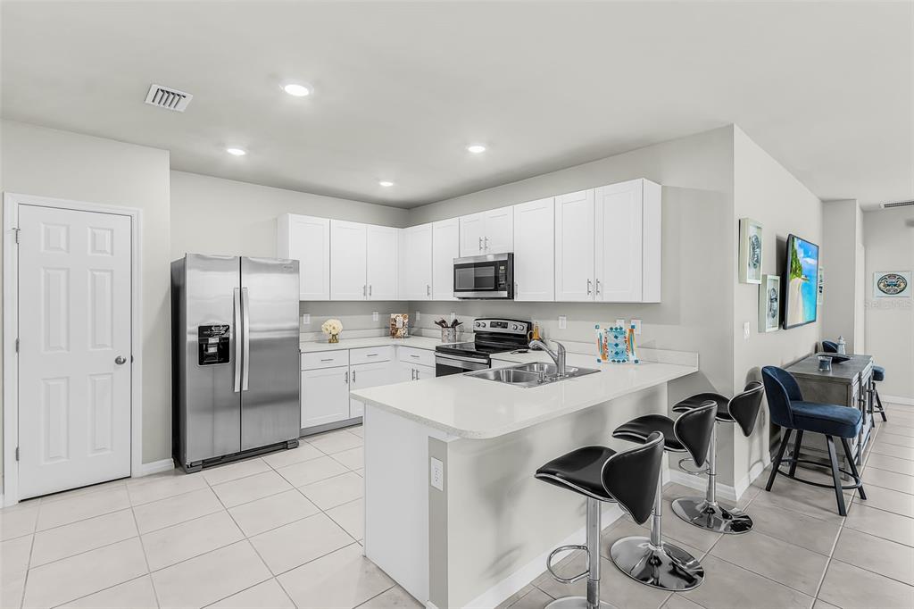 A modern kitchen features white cabinetry, stainless steel appliances, and a breakfast bar with stools — 25008 E LENOX CIRCLE, PUNTA GORDA, FL