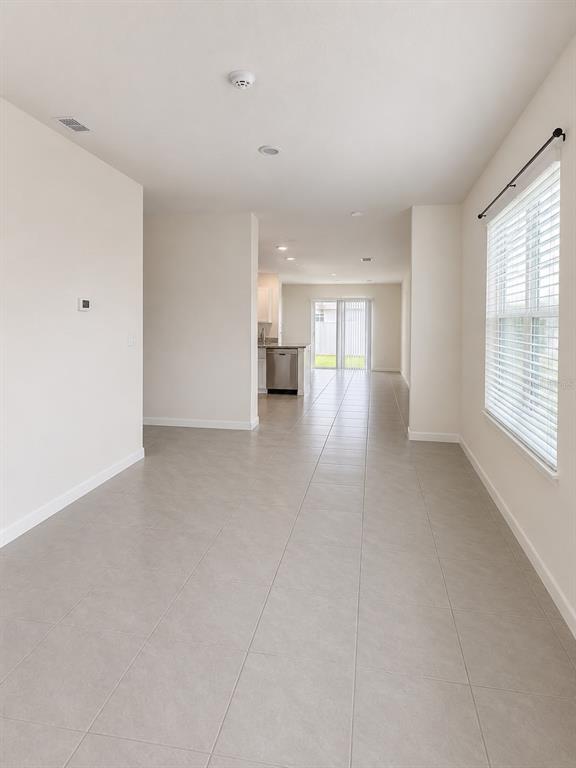 An open-concept room with light-colored tile flooring leads to a kitchen and sliding glass doors — 7171 CARIB GRACKLE DRIVE, HARMONY, FL
