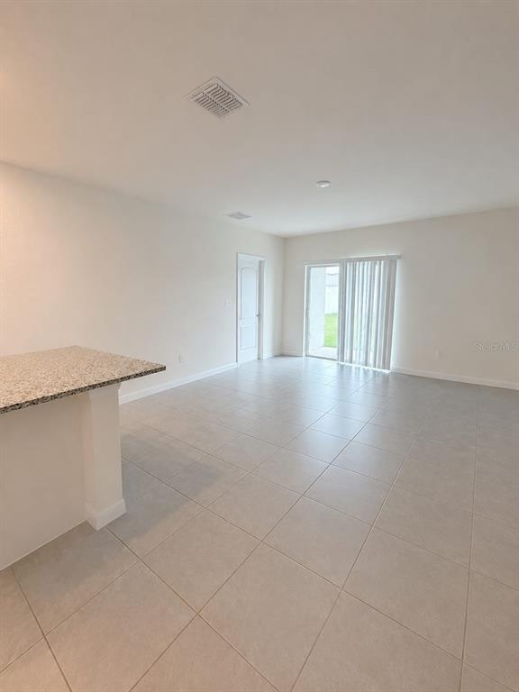 An open-concept room features light-colored tile flooring, a granite-topped island, and sliding glass doors — 7171 CARIB GRACKLE DRIVE, HARMONY, FL