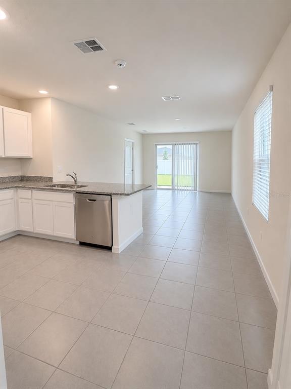 A kitchen with white cabinets and a stainless steel dishwasher opens into a tiled living area — 7171 CARIB GRACKLE DRIVE, HARMONY, FL