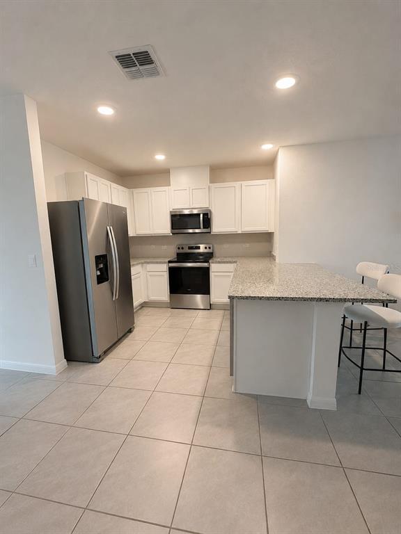 A kitchen features white cabinets, stainless steel appliances, granite countertops, and light tile flooring — 7171 CARIB GRACKLE DRIVE, HARMONY, FL