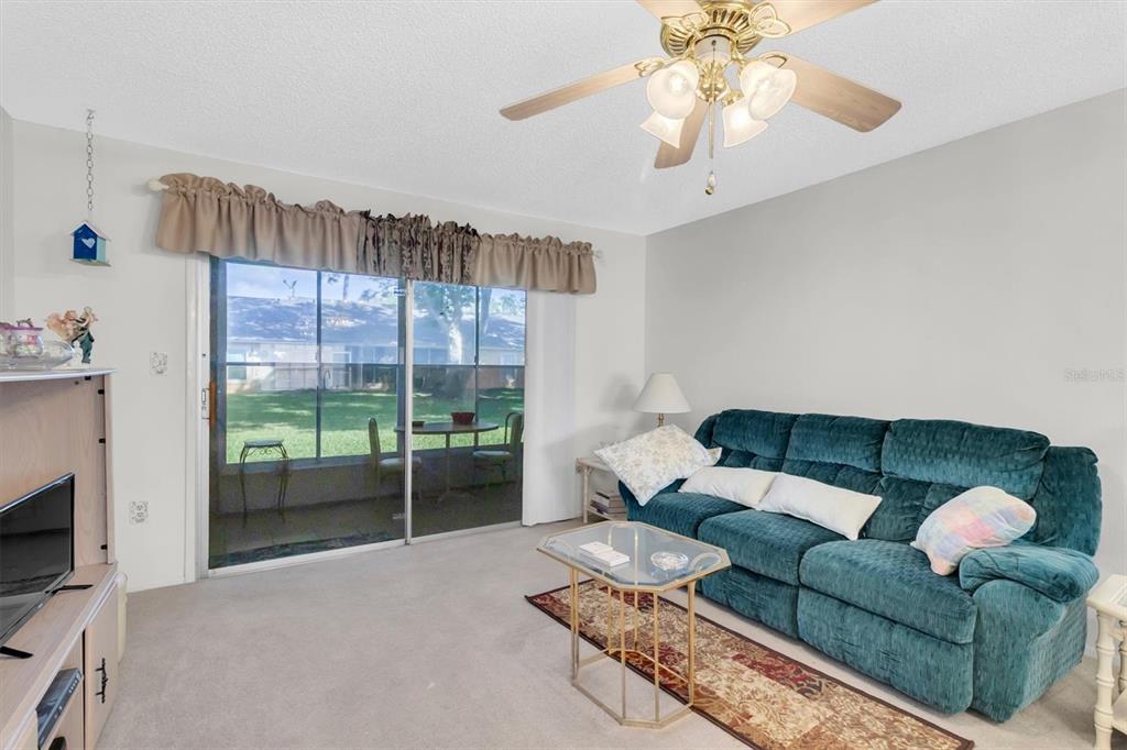 A living room features a teal sofa, glass coffee table, ceiling fan, and sliding glass doors — 4968 GRIST MILL CIRCLE, NEW PORT RICHEY, FL