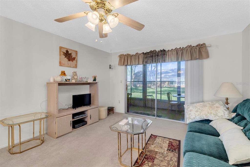 A living room features a teal sofa, glass-topped tables, a television console, and sliding glass doors — 4968 GRIST MILL CIRCLE, NEW PORT RICHEY, FL