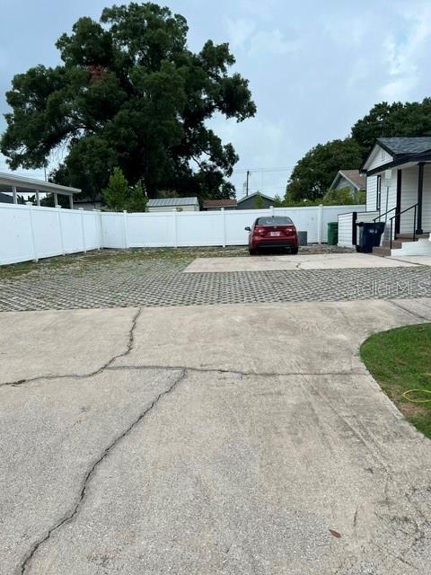 A red car is parked on a paved driveway in front of a white fence — 1202 N ARMENIA AVENUE, TAMPA, FL