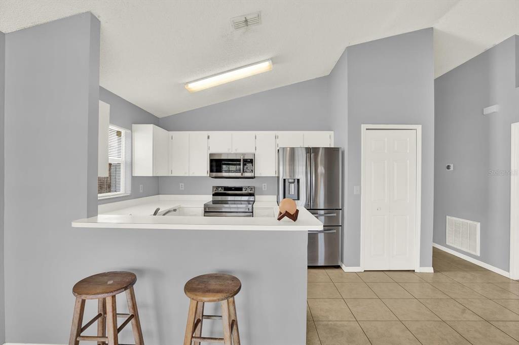 A kitchen with white cabinets, stainless steel appliances, and a breakfast bar with two stools — 1618 CITRUS ORCHARD WAY, VALRICO, FL