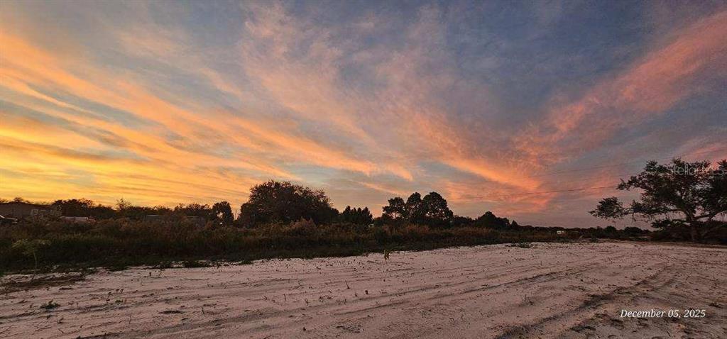 A sandy, undeveloped lot is shown under a vibrant sunset sky with scattered trees — 18398 NW 286TH STREET, OKEECHOBEE, FL