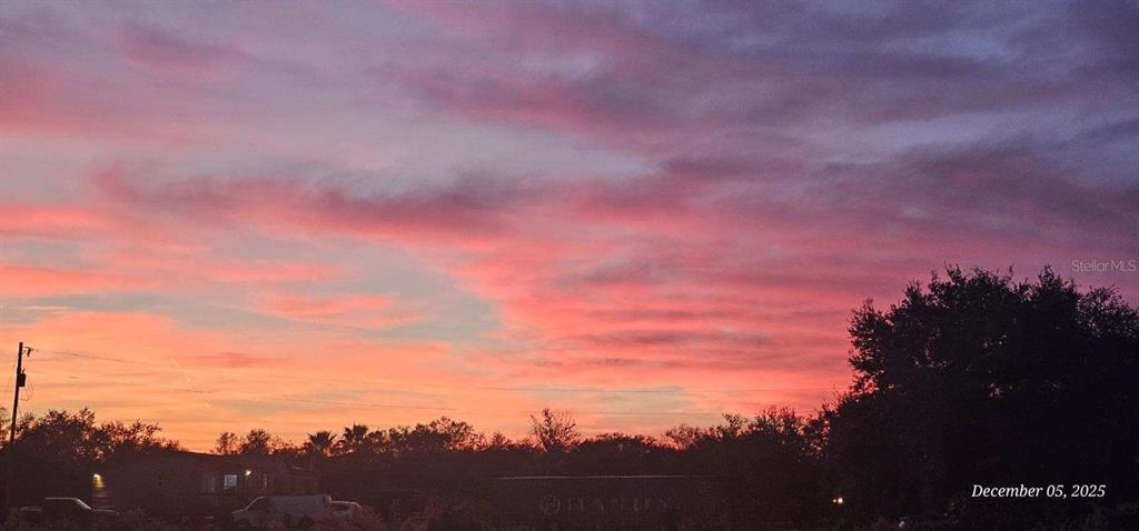 A vibrant sunset sky glows with shades of pink and orange above a dark treeline — 18398 NW 286TH STREET, OKEECHOBEE, FL