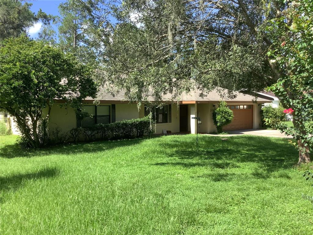 A single-story house with a tan exterior, a two-car garage, and a large front lawn — 34473 ORCHID PARKWAY, RIDGE MANOR, FL