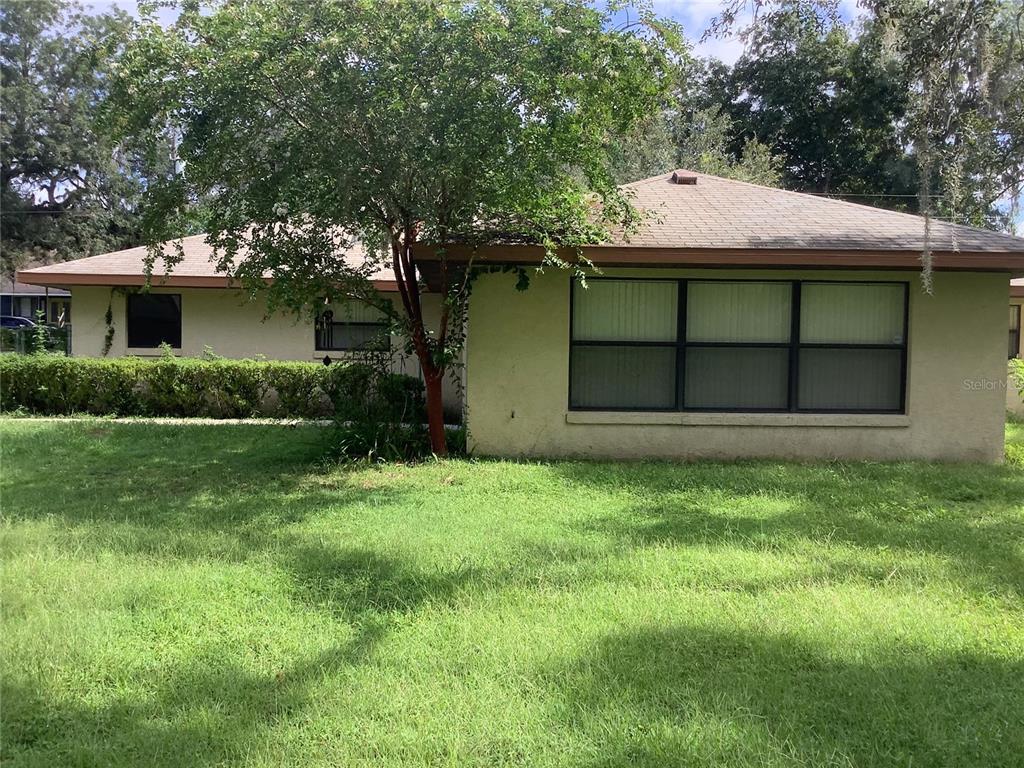 A single-story house with a beige stucco exterior, a brown roof, and a large front lawn — 34473 ORCHID PARKWAY, RIDGE MANOR, FL