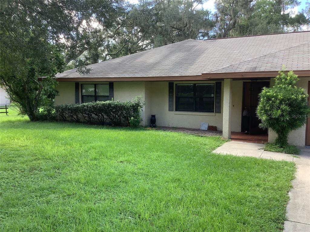 A single-story house with a tan stucco exterior, a brown roof, and a front lawn — 34473 ORCHID PARKWAY, RIDGE MANOR, FL