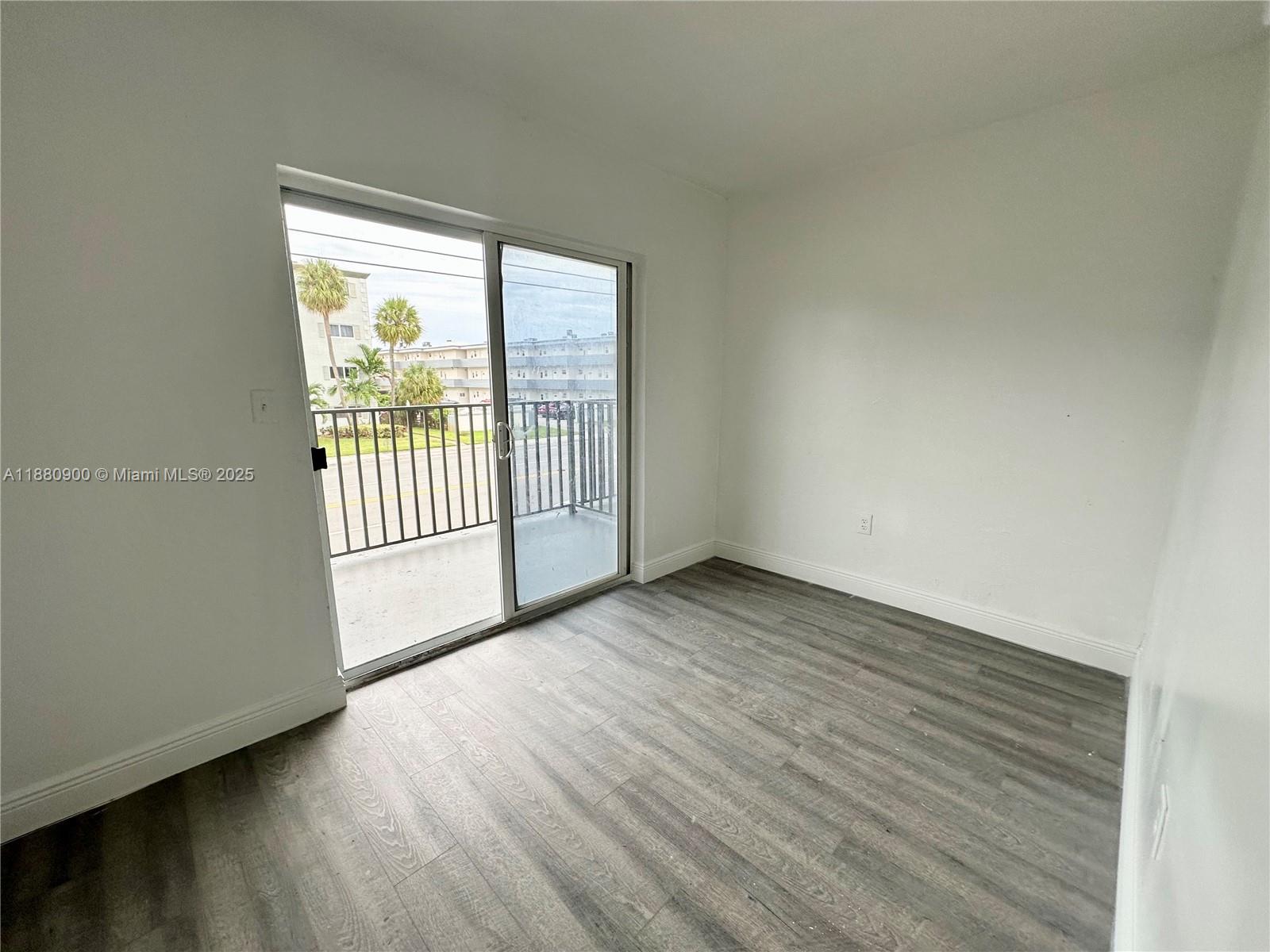 A room with gray wood-look flooring and a sliding glass door leading to a balcony — 13285 NE 6th Ave # 401, North Miami FL 33161, NORTH MIAMI, FL