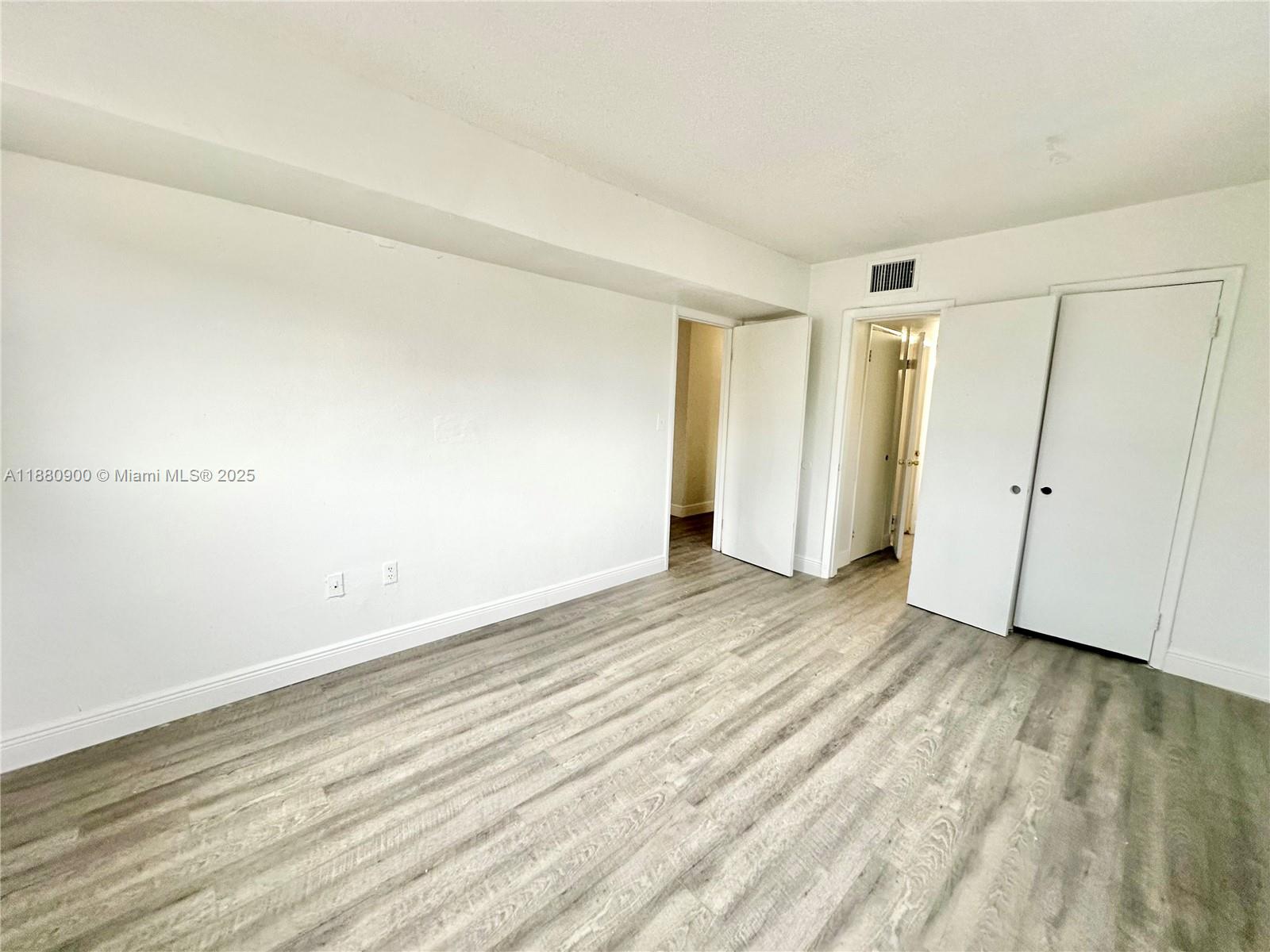 An empty room features white walls, light wood-look flooring, and two sets of closet doors — 13285 NE 6th Ave # 401, North Miami FL 33161, NORTH MIAMI, FL