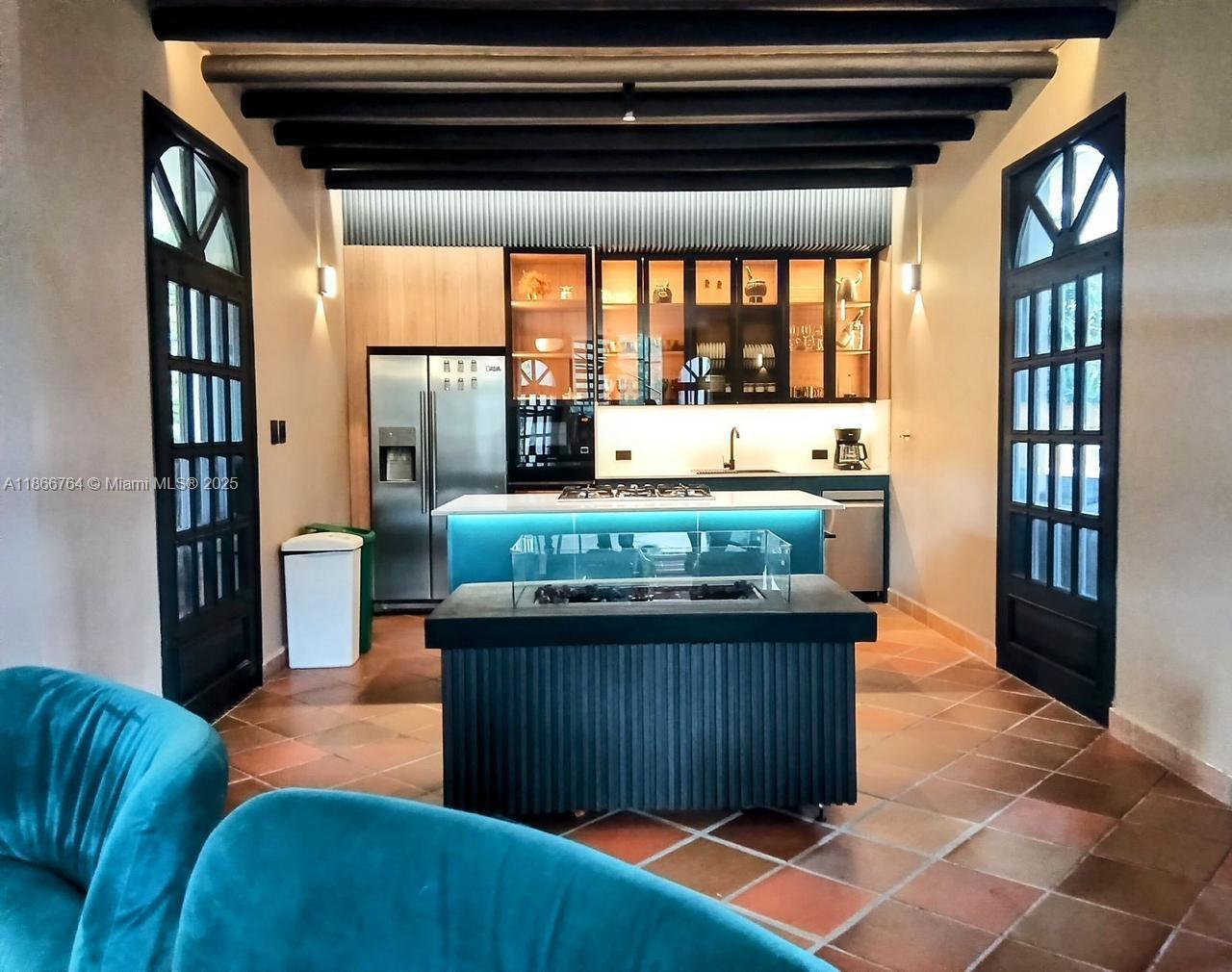 A kitchen features a central island with a glass fireplace, teal lighting, and terracotta flooring — Lote 4 Vereda La Honda, At 054, At