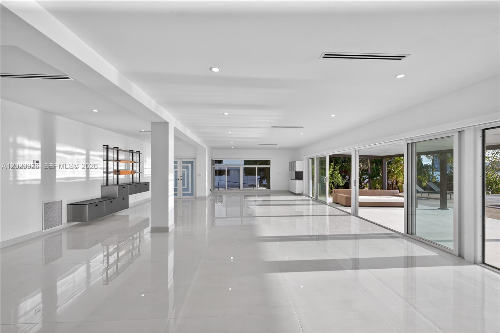 A spacious, minimalist room features white tile floors, recessed lighting, and large sliding glass doors — 1101 S Shore Dr # 1, Miami Beach FL 33141, MIAMI BEACH, FL