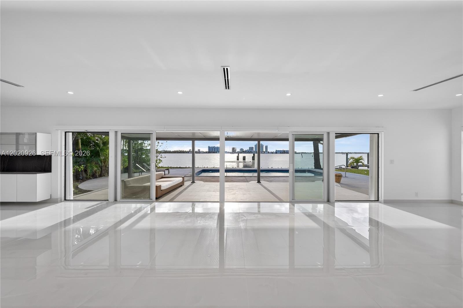 A bright, minimalist living space with white tile floors opens to a pool and waterfront — 1101 S Shore Dr # 1, Miami Beach FL 33141, MIAMI BEACH, FL