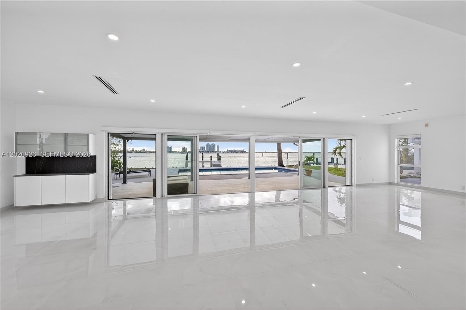 A minimalist white room features large sliding glass doors opening to a pool and waterfront — 1101 S Shore Dr # 1, Miami Beach FL 33141, MIAMI BEACH, FL