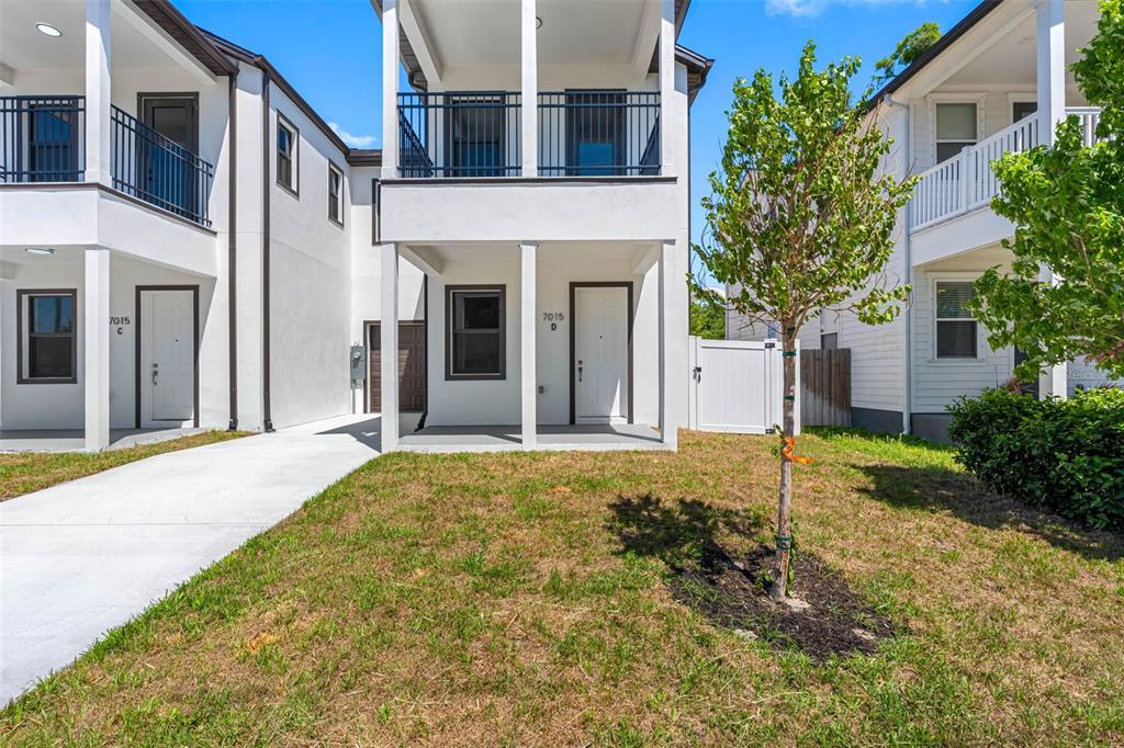 A two-story white townhouse exterior with a covered porch, balcony, and a small front yard — 7015 N CENTRAL AVENUE Unit D, TAMPA, FL