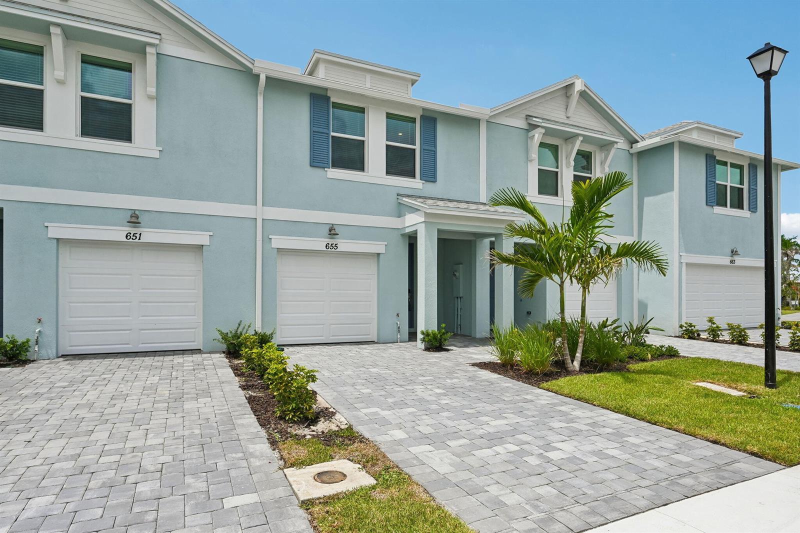 A row of light blue townhouses features white garage doors, paved driveways, and a palm tree — 655 Salisbury Circle, Fort Pierce FL 34982, FORT PIERCE, FL