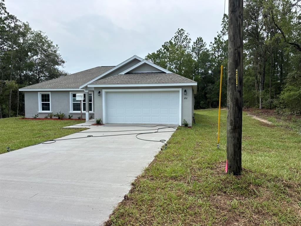 A single-story house with a white garage door and a concrete driveway sits on a lot — 892 W CADIMA PLACE, DUNNELLON, FL