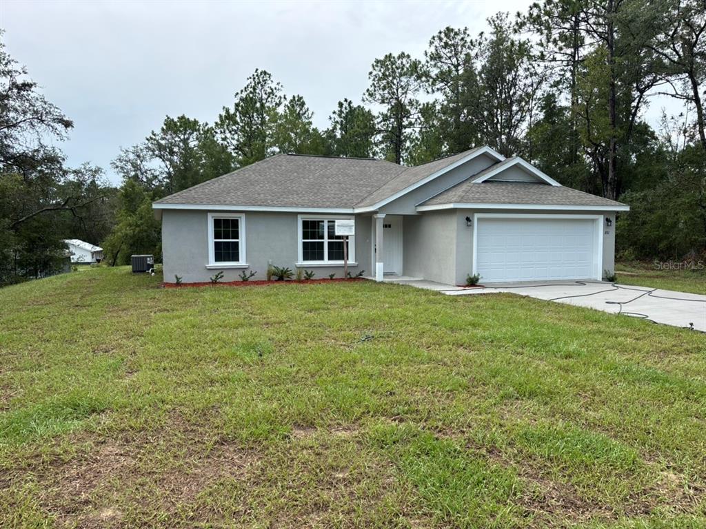 A single-story house with a gray stucco exterior, a two-car garage, and a grassy yard — 892 W CADIMA PLACE, DUNNELLON, FL