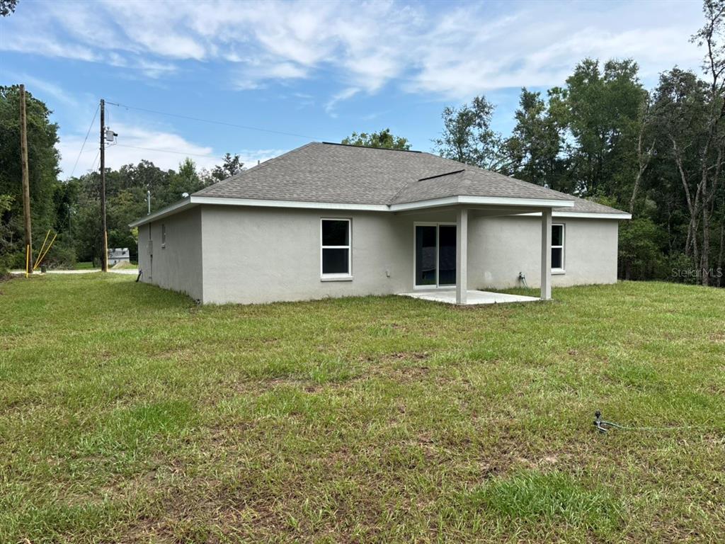 The rear exterior of a single-story house with a covered patio and a grassy yard — 892 W CADIMA PLACE, DUNNELLON, FL