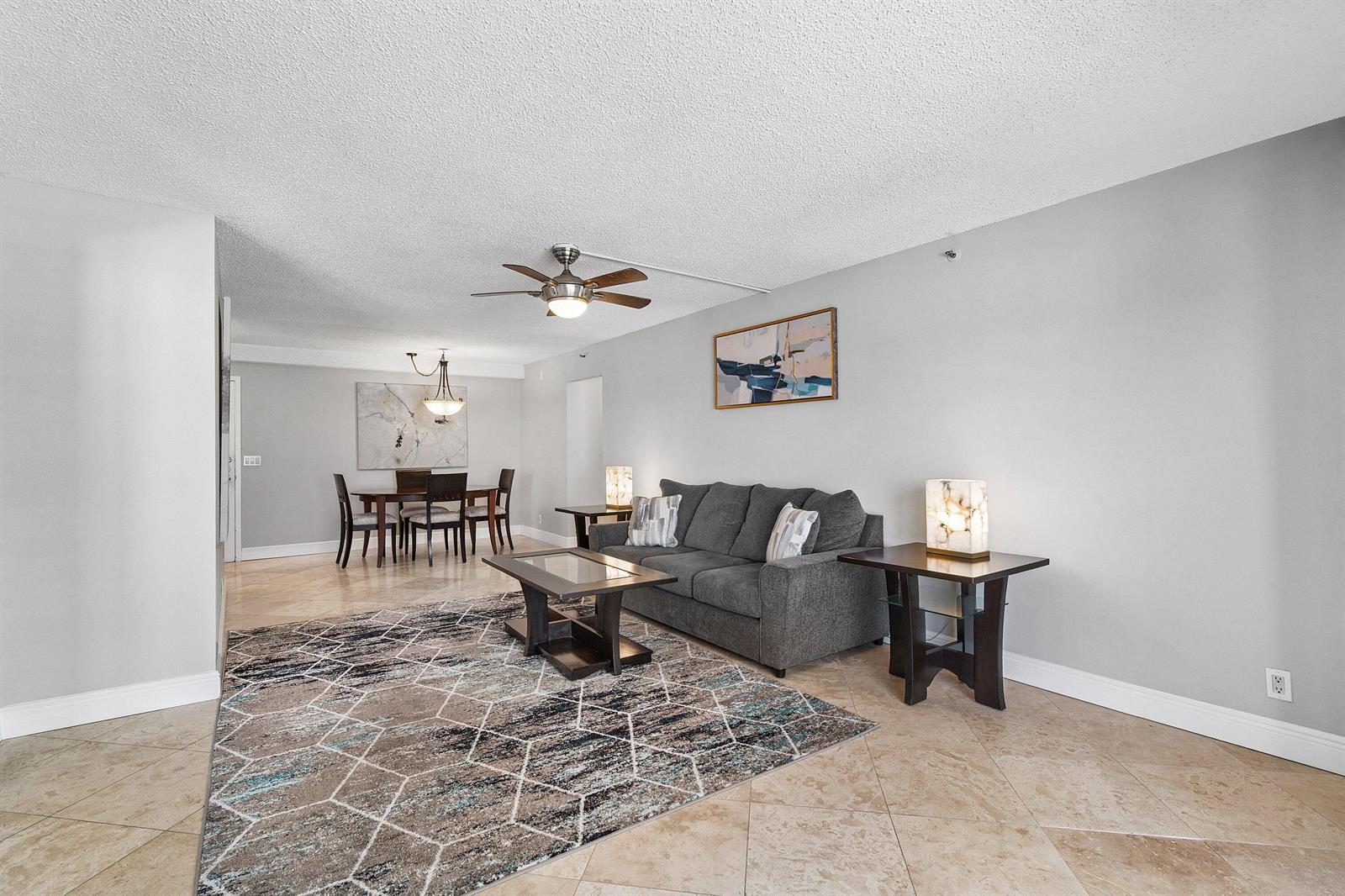 A living room and dining area feature tile floors, a gray sofa, and area rug — 4511 S Ocean Boulevard # 106, Highland Beach FL 33487, HIGHLAND BEACH, FL