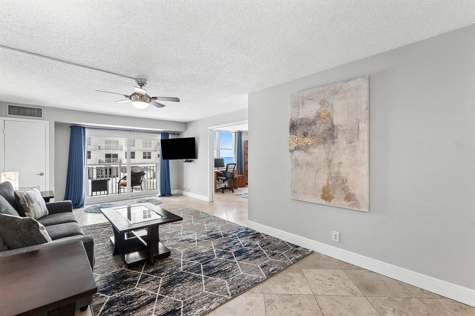A living room features a gray sofa, geometric rug, large abstract art, and balcony access — 4511 S Ocean Boulevard # 106, Highland Beach FL 33487, HIGHLAND BEACH, FL