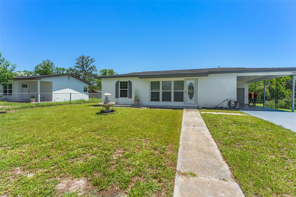 A white single-story house with a carport, a concrete walkway, and a front yard fountain — 1625 HASTINGS DRIVE, DELTONA, FL