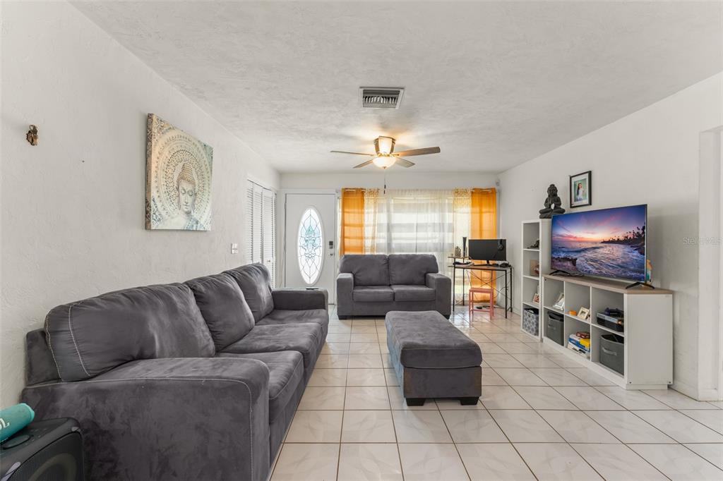 A living room features a grey sofa, matching ottoman, white tiled floors, and a television — 1625 HASTINGS DRIVE, DELTONA, FL