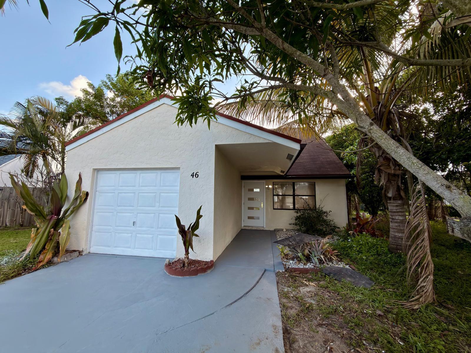 A single-story house with a white garage door, a front entrance, and surrounding tropical landscaping — 46 Tara Lakes Drive E, Boynton Beach FL 33436, BOYNTON BEACH, FL