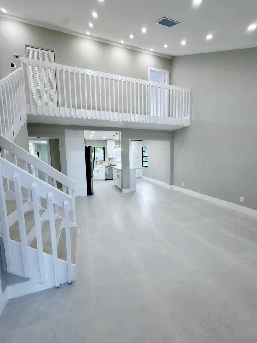 A bright, open-concept living area features a white staircase, a loft balcony, and tile flooring — 46 Tara Lakes Drive E, Boynton Beach FL 33436, BOYNTON BEACH, FL