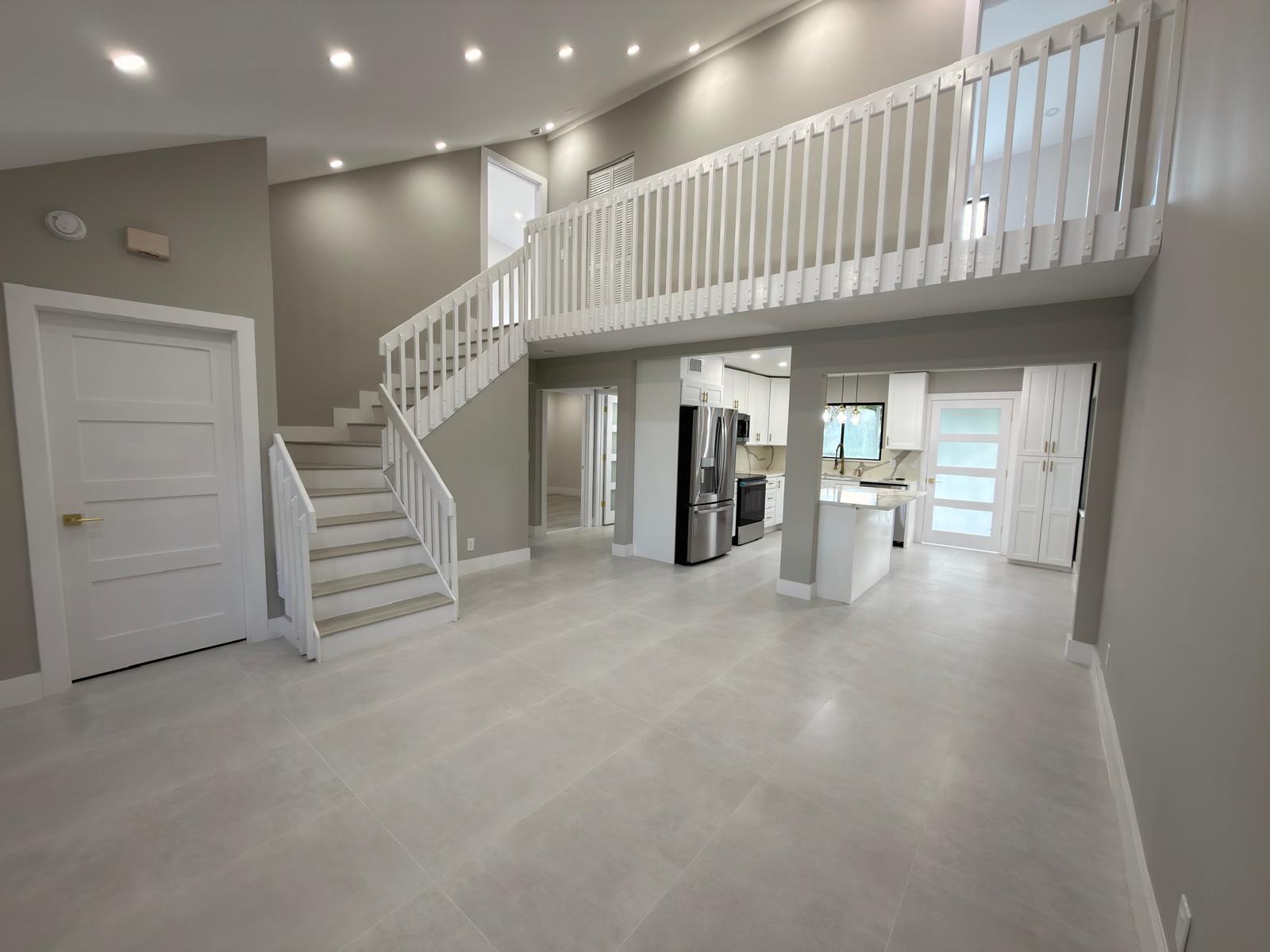 An open-concept living area features a staircase, a lofted balcony, and a modern white kitchen — 46 Tara Lakes Drive E, Boynton Beach FL 33436, BOYNTON BEACH, FL