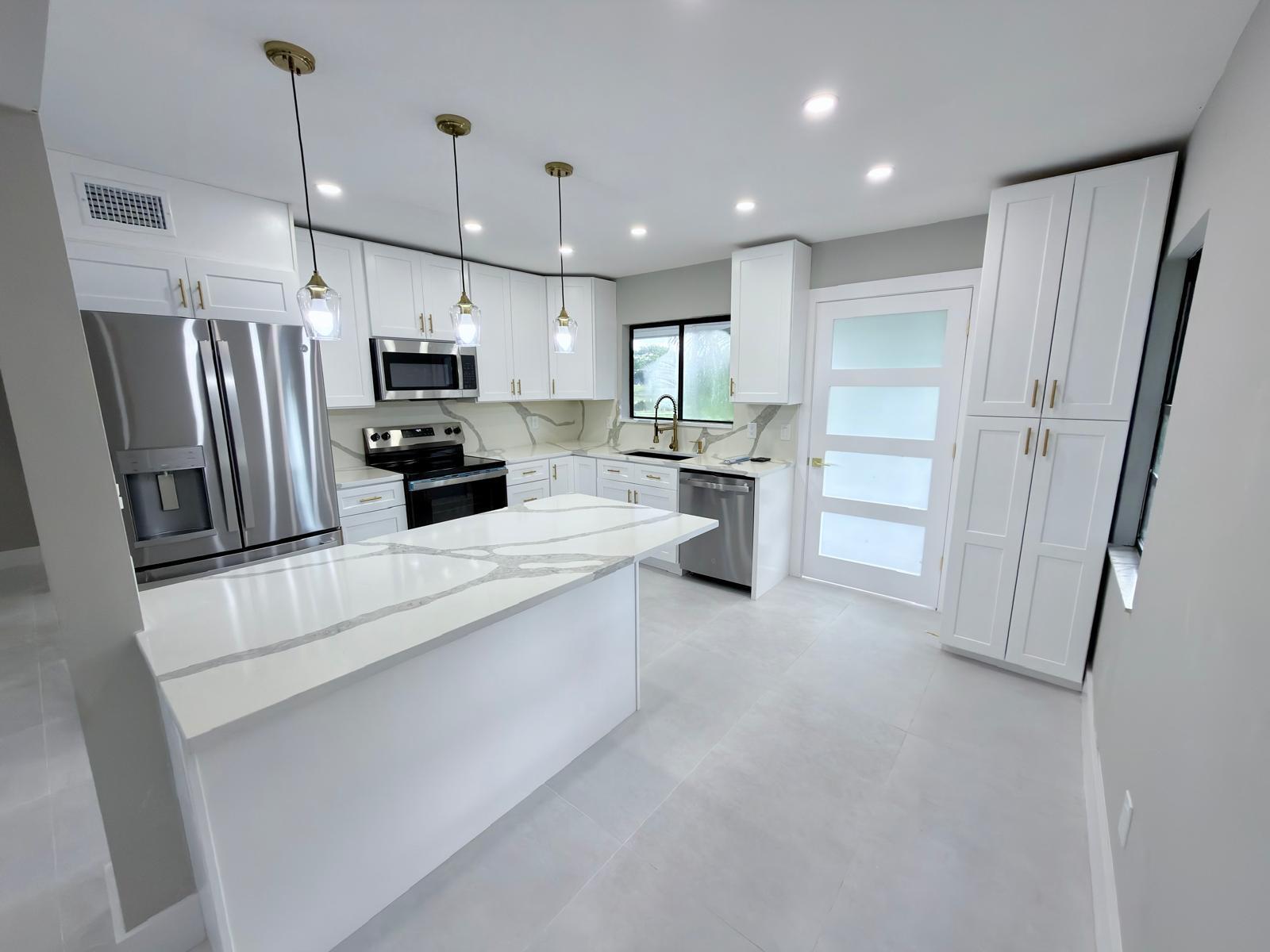 A modern kitchen features white cabinets, marble-patterned countertops, stainless steel appliances, and gold hardware — 46 Tara Lakes Drive E, Boynton Beach FL 33436, BOYNTON BEACH, FL