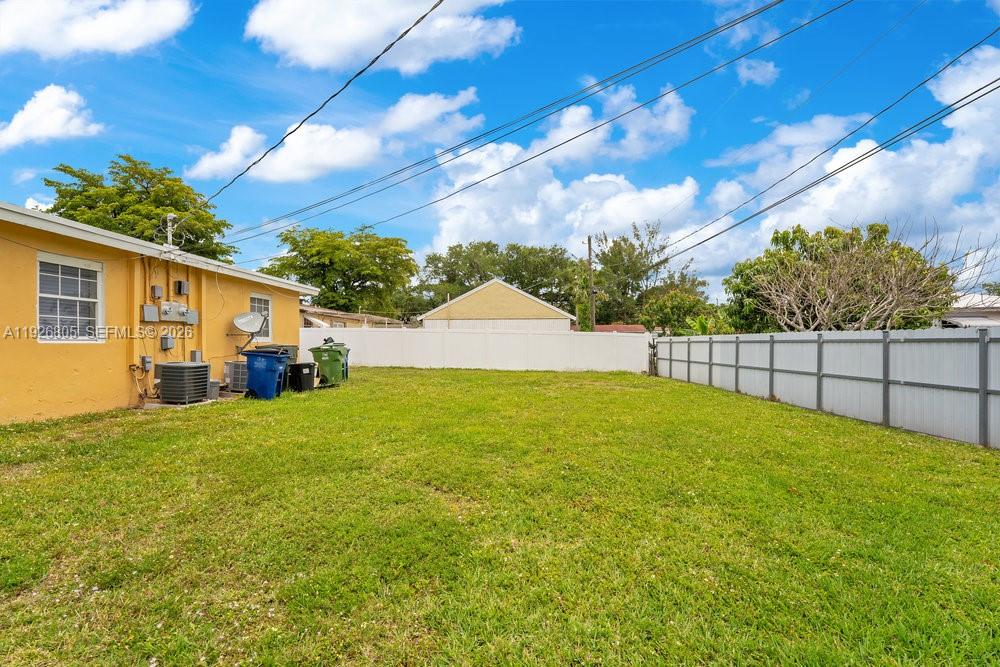 A grassy backyard features a yellow house exterior, a white fence, and utility equipment — 417 SW 3rd St, Hallandale Beach FL 33009, HALLANDALE BEACH, FL