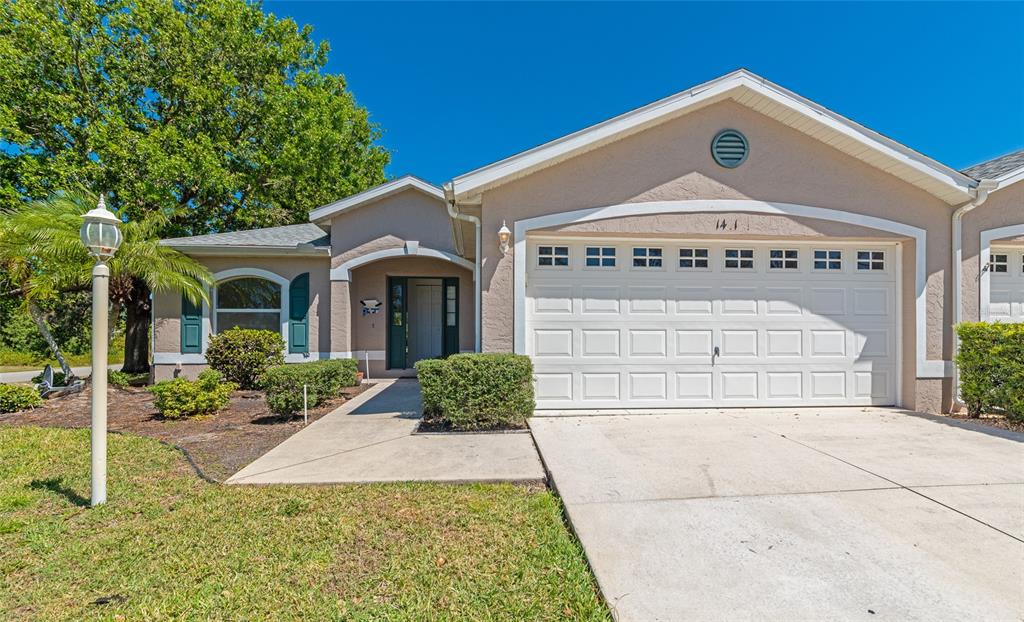 A single-story house with a beige stucco exterior, a two-car garage, and a concrete driveway — 1401 HEDGEWOOD CIRCLE, NORTH PORT, FL