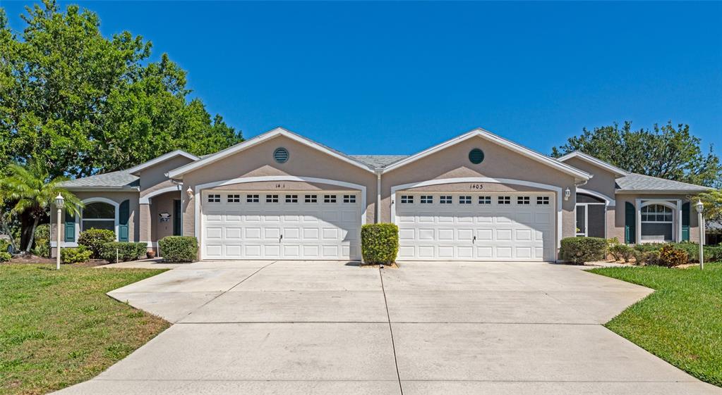 A single-story duplex with two white garage doors and beige stucco siding under a blue sky — 1401 HEDGEWOOD CIRCLE, NORTH PORT, FL
