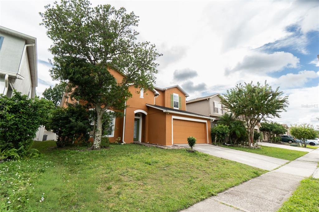 A two-story orange stucco house with a two-car garage and a large front tree — 7908 BEAR CLAW RUN, ORLANDO, FL
