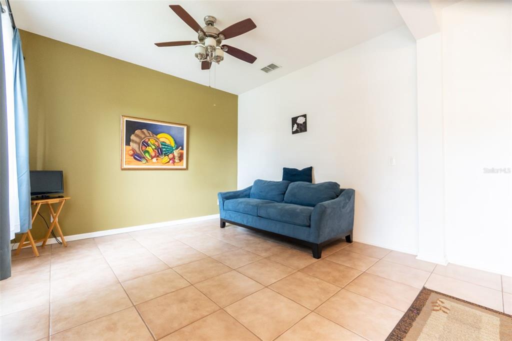 A living room features a blue sofa, a ceiling fan, and a framed wall painting — 7908 BEAR CLAW RUN, ORLANDO, FL