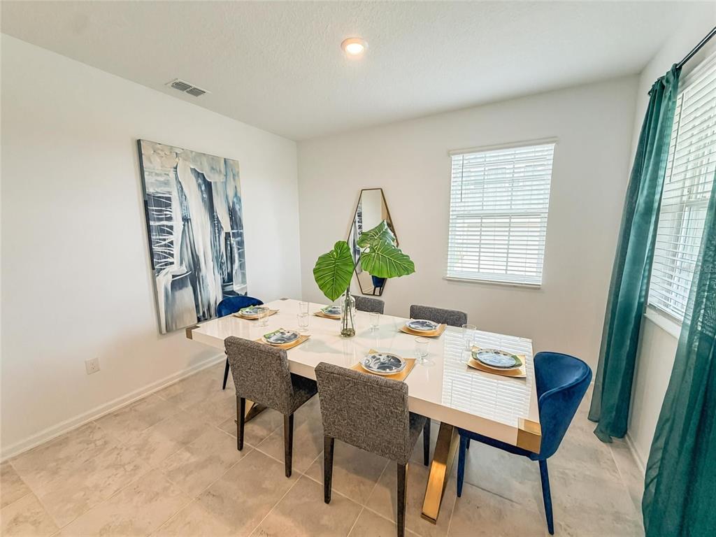 A dining room features a white table, gray and blue chairs, and large wall art — 1692 TOHOQUA BOULEVARD, KISSIMMEE, FL