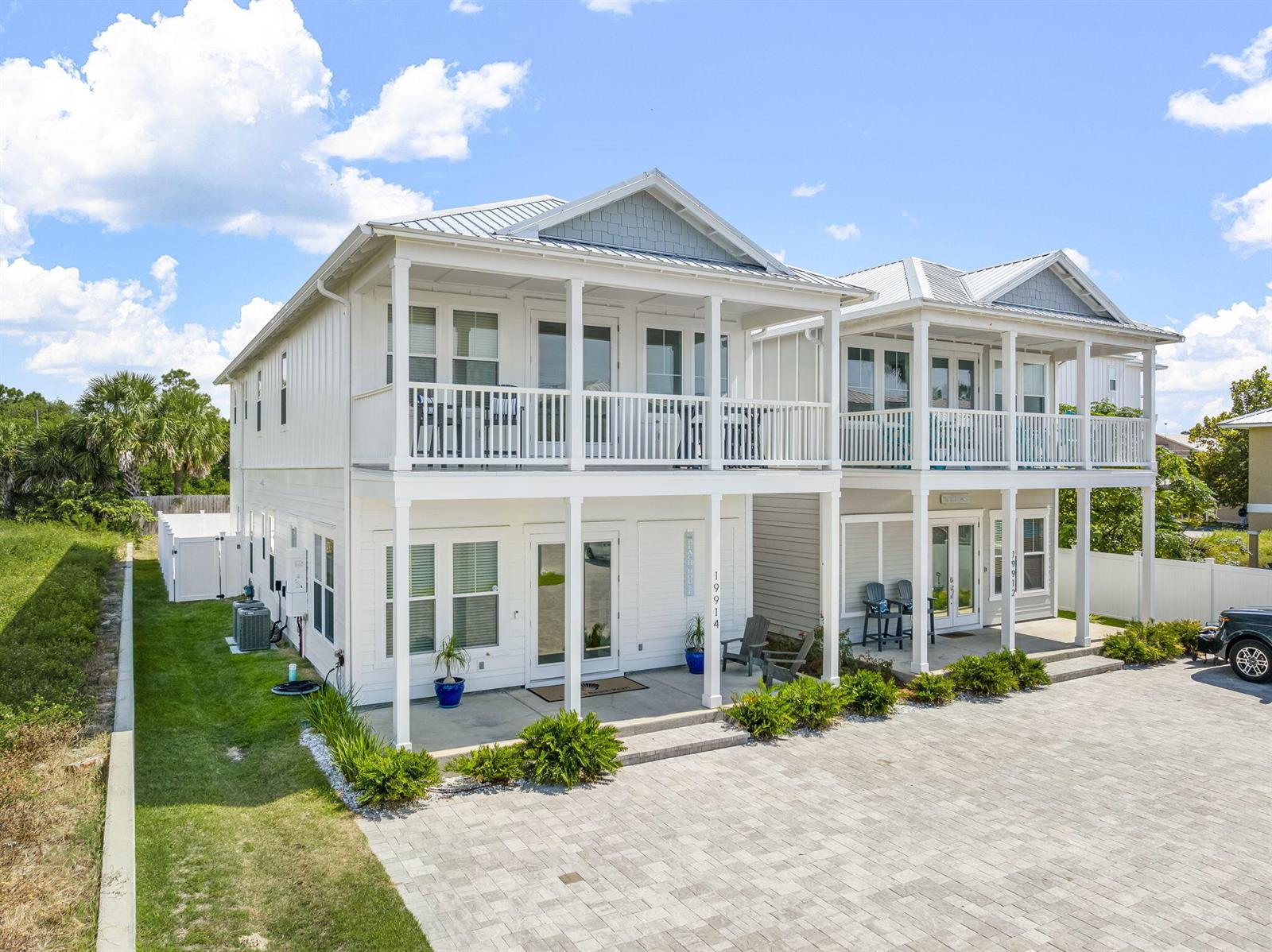 A two-story white duplex with covered porches and a paved driveway under a blue sky — 19914 Front Beach Road, FL 32413, FL