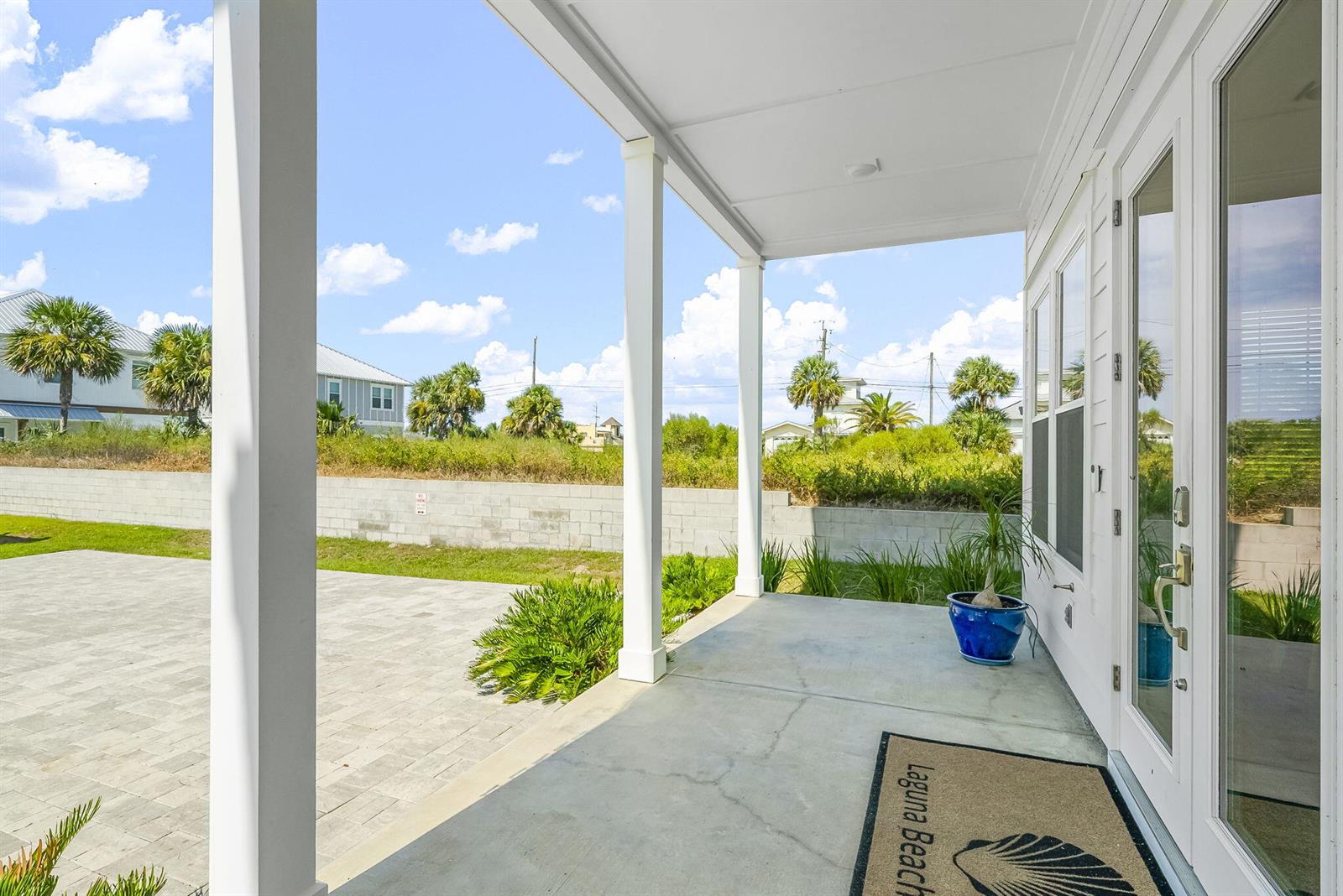 A covered concrete porch features white columns, a blue planter, and a Laguna Beach mat — 19914 Front Beach Road, FL 32413, FL